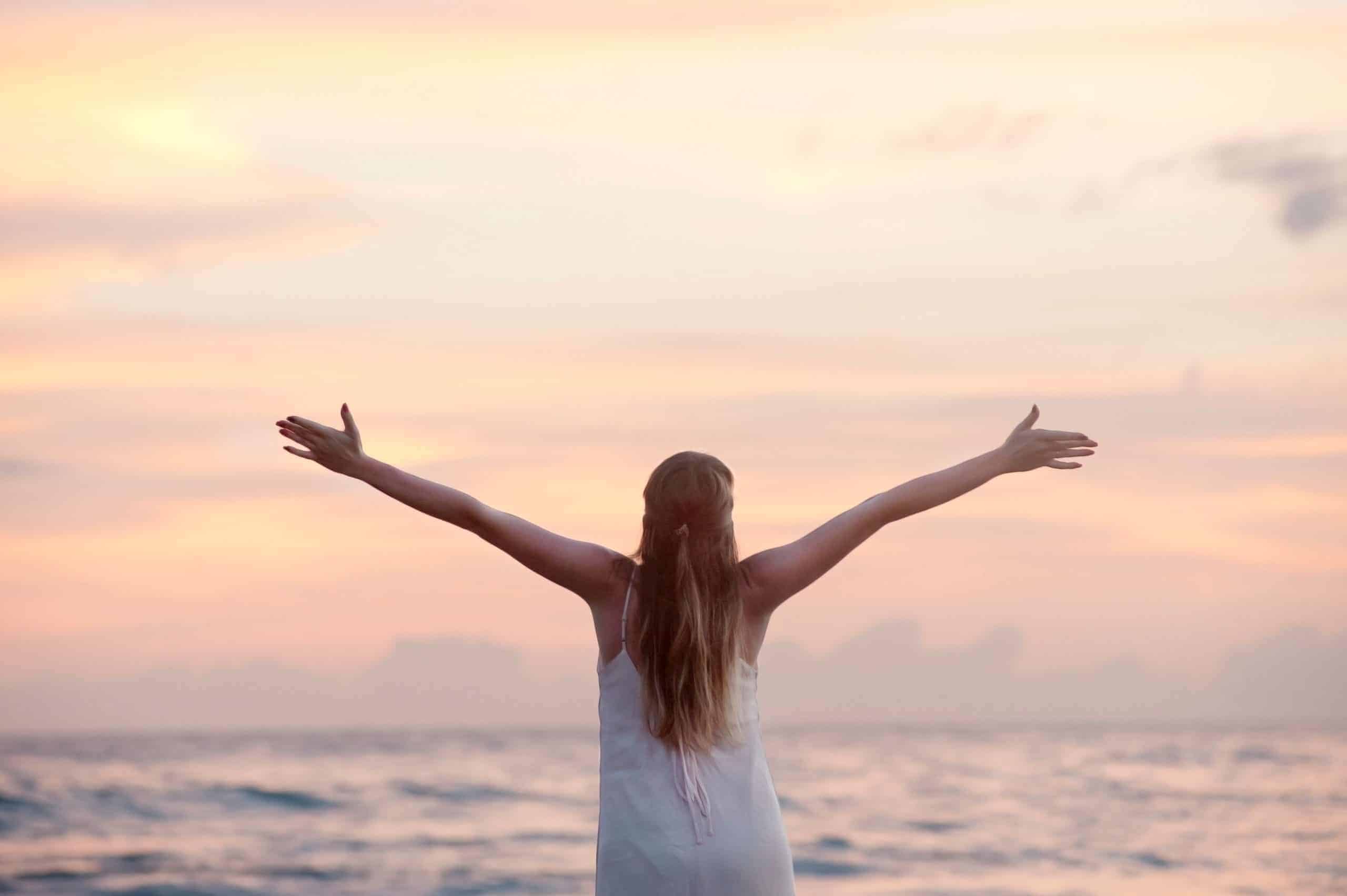 rear-view-of-woman-with-arms-raised-at-beach-during-sunset-320007