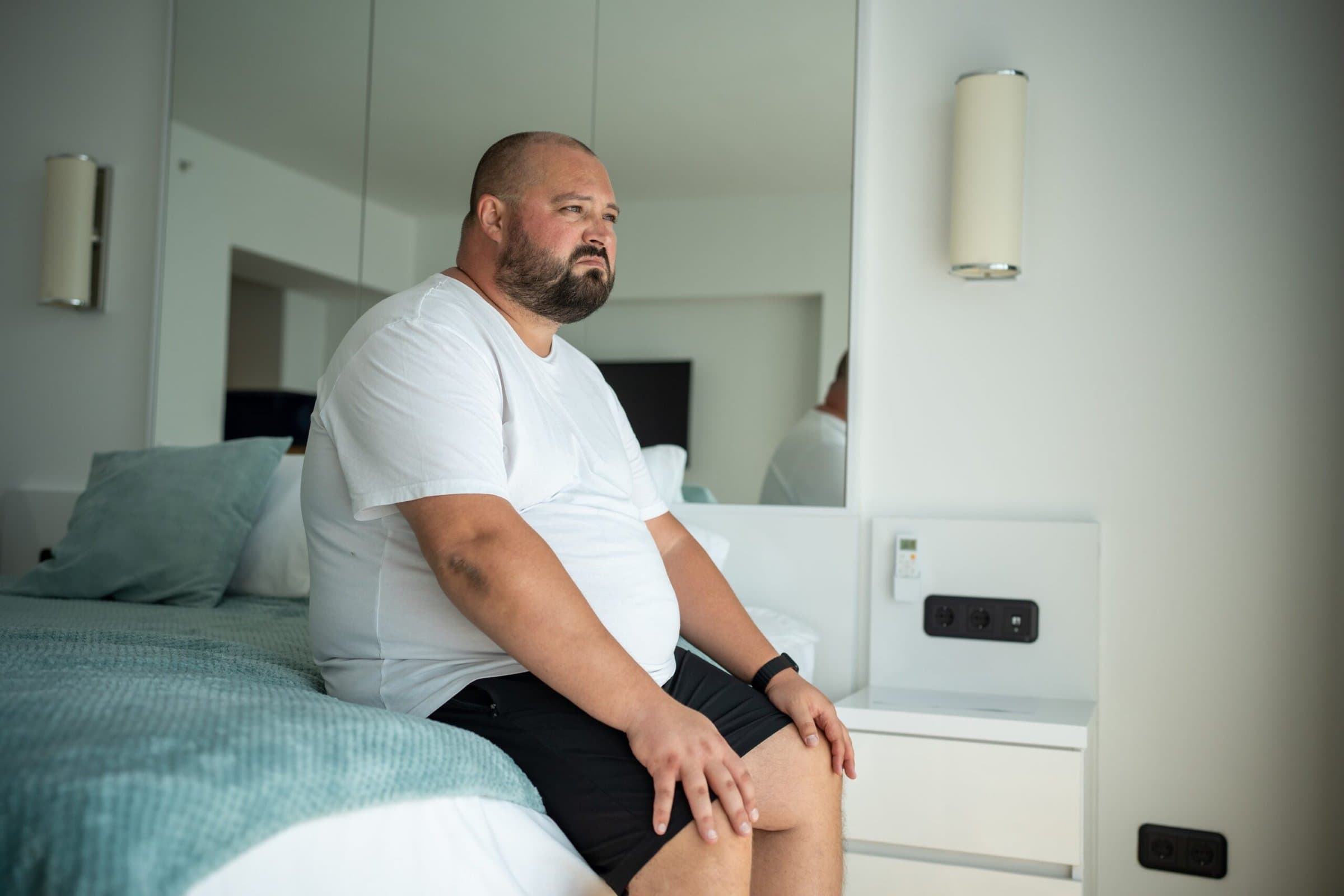 Obese,Guy,Sitting,On,Bed,With,Disgruntled,Face.,Overweight